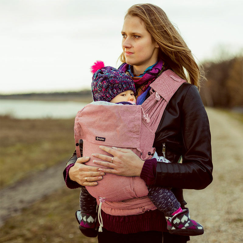 A woman standing at the beach on an autumn day wearing a black jacket, carrying her bobble hat-wearing baby in a Didymos Didyklick Chili baby carrier