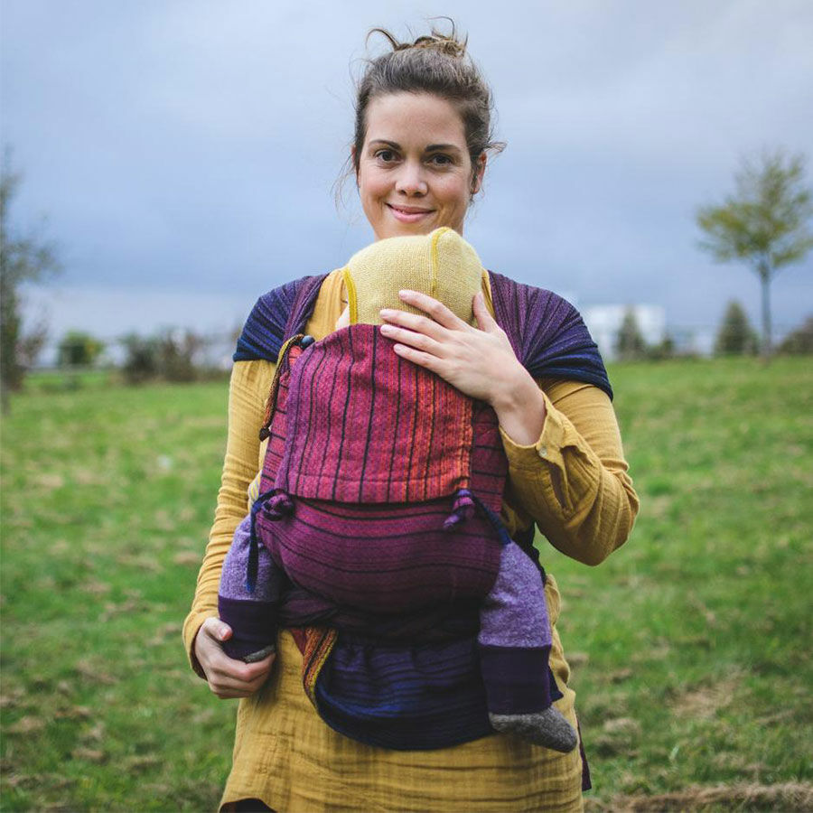 A woman standing in a field on a cloudy day carrying her baby on her front with in a Girasol WrapMysol Twilight