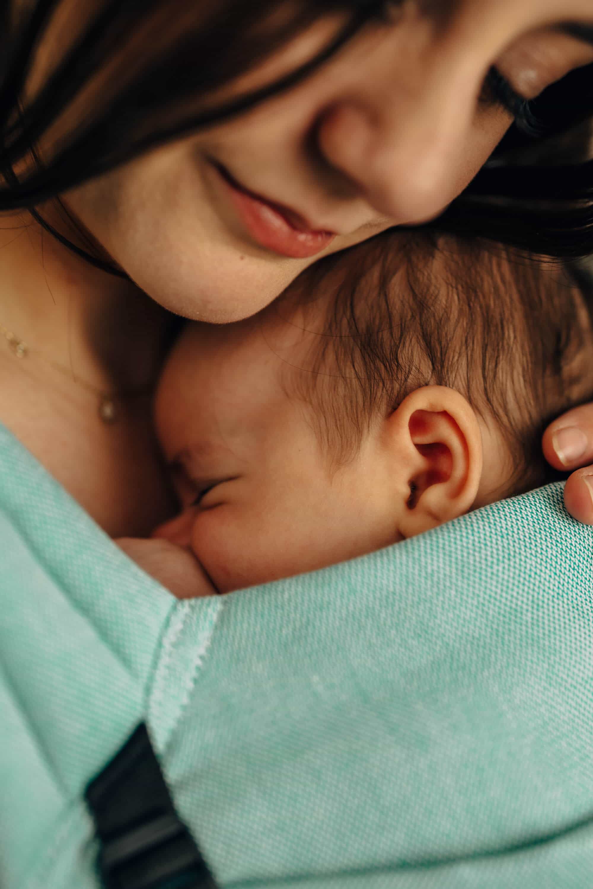 A closeup shot a woman with brown hair snuggling her young baby in a Lennylight Agave baby carrier.