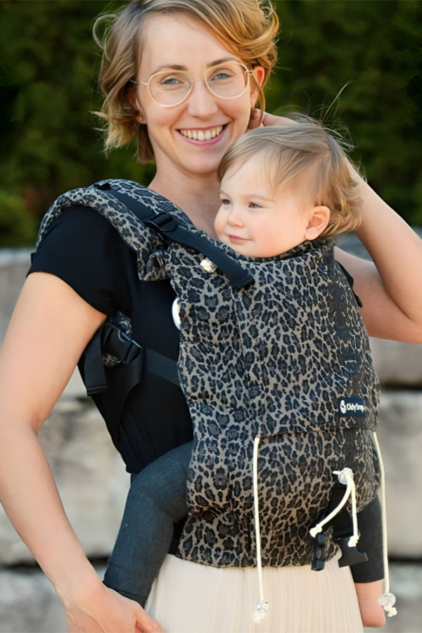 A woman with brown hair carrying her young baby in a Didymos Didyklick baby carrier.