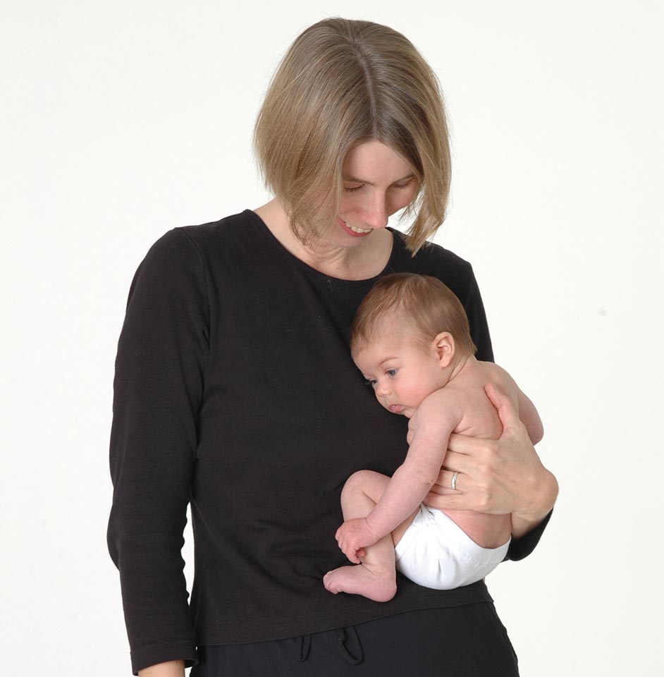 Anna from the company Didymos holding a baby in the crook of her left arm, showing baby's naturally tucked position.