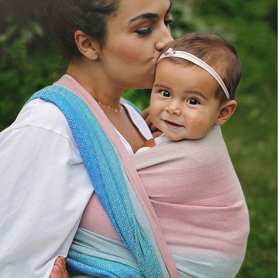 A woman kissing the top of her baby's head whilst carrying her in a Little Frog Elafonisi baby wrap.
