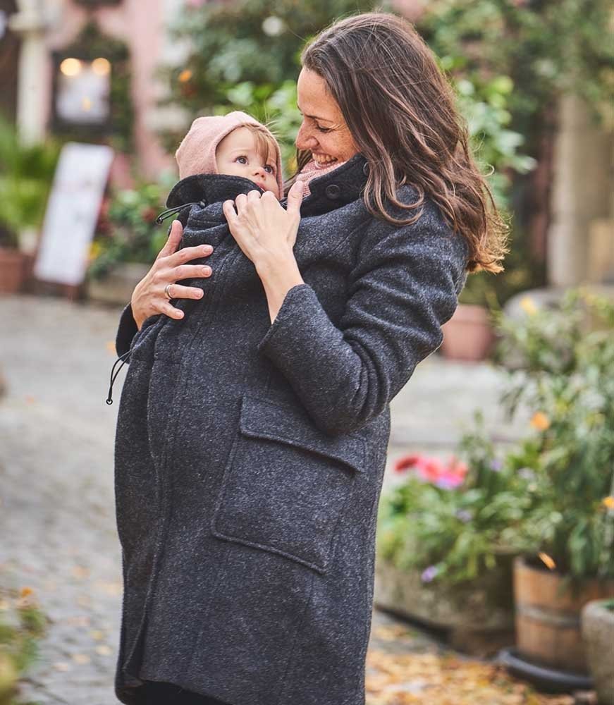 A woman with long brown hair smiling at her baby whom she is carrying in a sling on her front whlist wearing the Mamalila Vienna Wool Hooded Coat